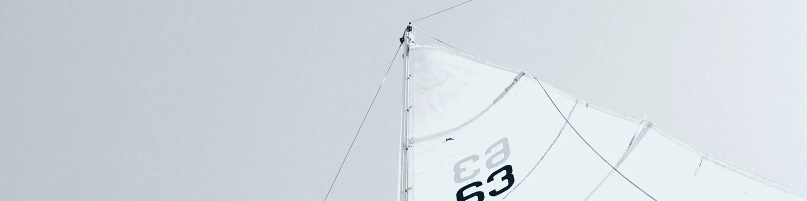 Zeil van een zeilboot tegen een grijze lucht